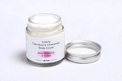 Glass jar open with metal lid showing luxury black raspberry and vanilla body cream