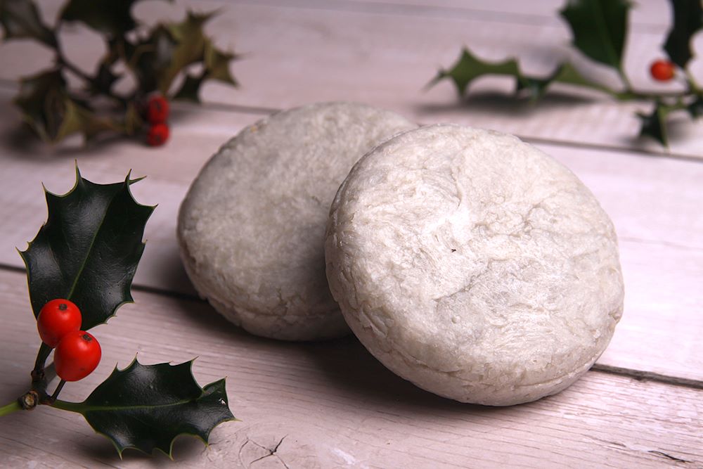Silvery white shampoo bars fragranced with winter berries. Shown with sprigs of holly